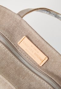 Bežna platnena torba s vidljivim metalnim patentnim zatvaračem, kožnom oznakom s natpisom "Vanessa Bruno" i ušivenim detaljima. Glatka tekstura i jednostavan dizajn.