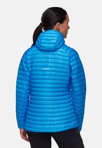 Blå isolerad jacka med huva, med ett quiltat mönster och logotyp på ryggen, tillverkad av ett slätt, lätt material.