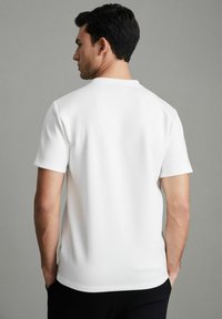 Camiseta blanca de manga corta hecha de una tela suave, con cuello redondo y un corte relajado, con costuras visibles en el dobladillo.