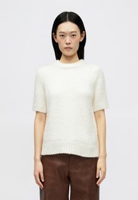 Pull en laine crème à manches courtes avec un ourlet côtelé et un col arrondi, présentant un motif de tricot texturé et une coupe décontractée.