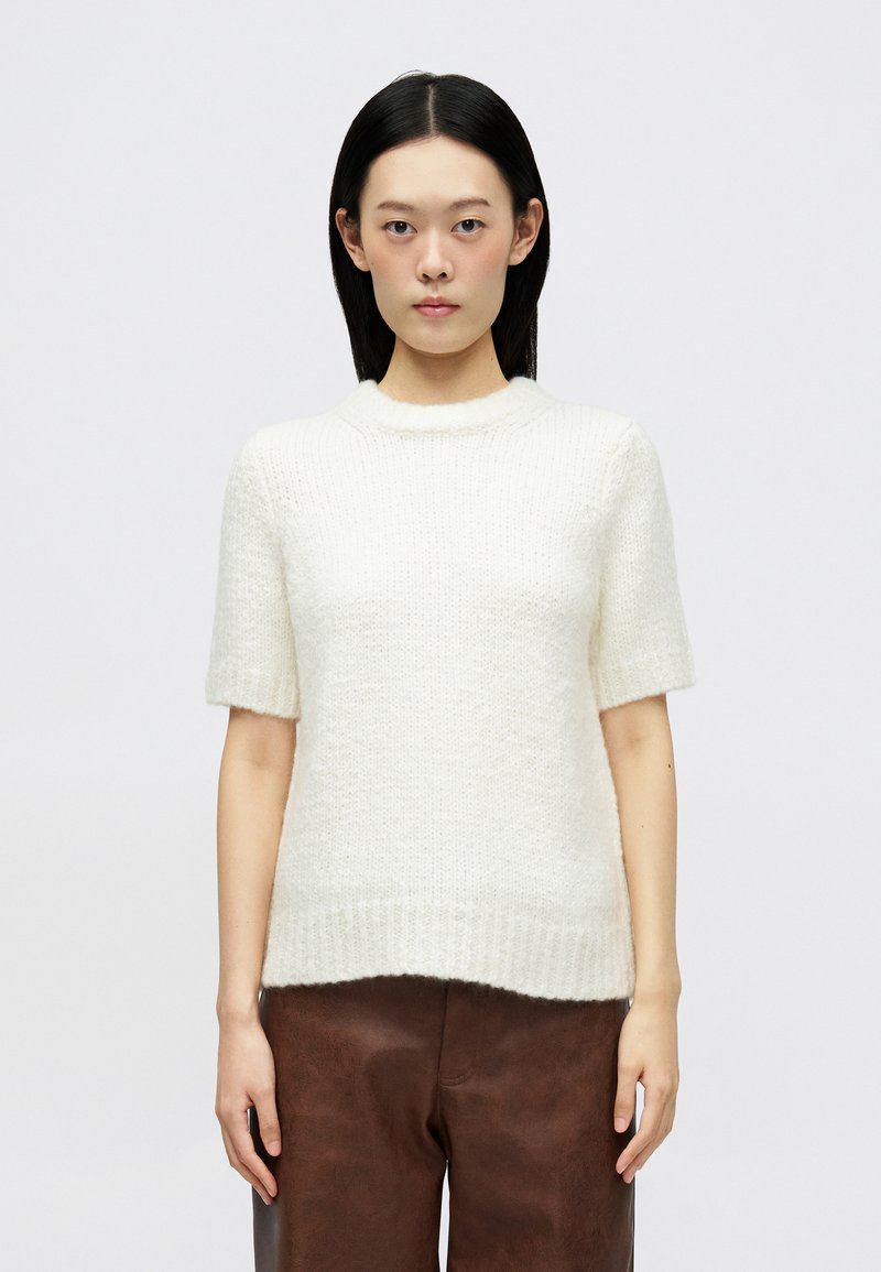 Pull en laine crème à manches courtes avec un ourlet côtelé et un col arrondi, présentant un motif de tricot texturé et une coupe décontractée.