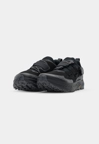 Black athletic shoes with a textured mesh upper, padded collar, and rugged rubber sole. Features a single fastening strap and a pull tab.