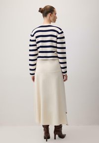 Prugasta pletena navy i bijela krojena zimska jakna, uparena s krem suknjom do poda. Smeđi čizmi do koljena s oštrim vrhom.