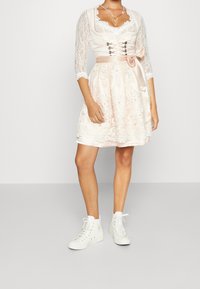 Robe rose clair avec des manches trois-quarts en dentelle, un corsage brodé, des accents en dentelle et un ruban en satin à la taille, assortie à des baskets montantes blanches.