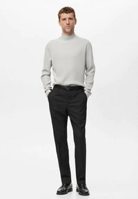 Jersey de canalé gris claro con cuello alto, combinado con pantalones negros a medida y zapatos negros de cordones. Silueta simple y estructurada.