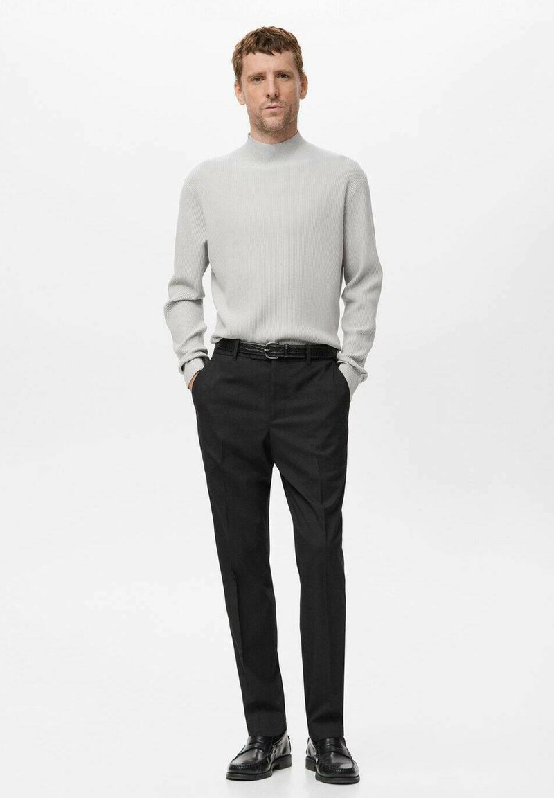 Light gray ribbed sweater with a mock neck, paired with tailored black trousers and black lace-up shoes. Simple, structured silhouette.