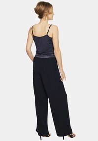 Granatowy kombinezon z dopasowanym elastycznym pasem, szerokimi nogawkami i cienkimi regulowanymi ramiączkami. Gładka faktura i minimalistyczny styl.