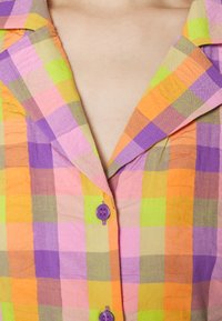 Camisa colorida de manga curta feita de tecido leve, com um padrão quadriculado em rosa, laranja, verde e púrpura, com botões púrpuras.