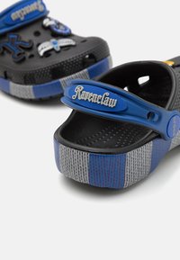 Black and blue Crocs featuring a Ravenclaw strap, textured sides, decorative elements, and a dual-tone blue and gray pattern.