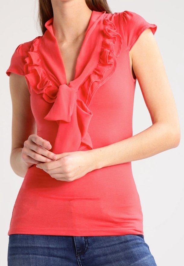 Coral top with a ruffled V-neck, short sleeves, and a tie detail at the neckline. Material appears smooth and stretchy.