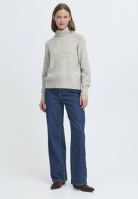 Svijetlo siva vuna turtleneck pulover s rebrastim izrezom, u kombinaciji s hlačama širokih nogavica tamnoplave boje viskog struka; model stoji okrenut prema naprijed.