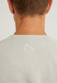 Sudadera gris claro con cuello redondo, textura acanalada y un detalle de costura distintivo en forma de flecha en la parte posterior.