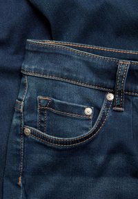 Ciemnoniebieskie dżinsy z przodu z kieszenią, kontrastującym brązowym szwem i srebrnymi detalami. Teksturowana tkanina o gładkim wykończeniu.