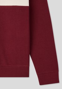 Felpa a maniche lunghe color bordeaux con polsini e orlo a costine, caratterizzata da una striscia bianca vicino alla parte superiore.