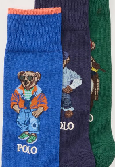 Τρεις πολύχρωμες κάλτσες με κεντημένες αρκούδες που φορούν καθημερινά ρούχα και γυαλιά ηλίου, κάθε κάλτσα δείχνει τη λέξη "POLO" κοντά στην αρκούδα.