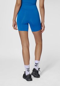 Blå atletiska shorts med ett mjukt, stretchigt tyg och en åtsittande design, kombinerade med svarta skor och vita strumpor med svarta chevronmönster.