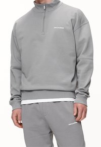 Felpa grigia con design a mezzo zip, polsini e orlo a coste. Presenta un piccolo logo sul petto, realizzato in tessuto testurizzato.