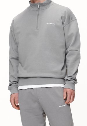 Felpa grigia con design a mezzo zip, polsini e orlo a coste. Presenta un piccolo logo sul petto, realizzato in tessuto testurizzato.