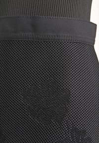 Černá sportovní tkanina s texturovanou mřížkou a hladkým pasem. Jemný květinový vzor embosovaný na povrchu mřížky.