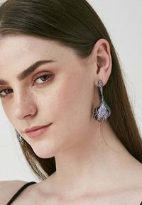 Svart och silver hängande örhängen med en vågig design, dekorerade med lila och klara rhinestones, som visar på intrikata detaljer och en glänsande finish.