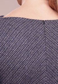 Tissu texturé marine avec un motif géométrique, comportant un discret zip au dos au niveau du col. Fini lisse.