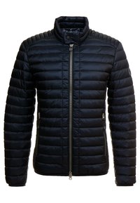 Marinblå vadderad jacka med ståkrage, dragkedjestängning och ribbad struktur. Har sido-fickor och en logotyp på ärmen.