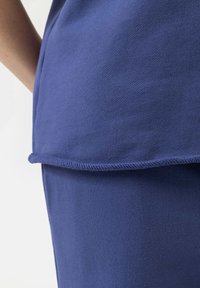 Blauwe katoenen stof met een gladde textuur, met een afgezoomde rand en subtiele stikdetails. De snit lijkt ontspannen en comfortabel.