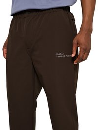 Close-up of dark brown pants with elastic waistband and side pockets, featuring a "HALO 1968197219" print on the right thigh.