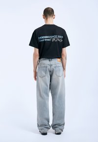Czarny t-shirt z krótkim rękawem z niebieskim napisem "DENIM SINCE 2004 (Dobre czasy)", w połączeniu z jasnoniebieskimi, luźnymi dżinsami.