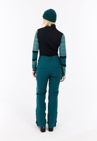 Een teal skikleding bestaat uit een zwart en aqua-gepatrooneerde lange mouw top, aangevuld met bijpassende teal broek met ritsaccents en een getailleerd ontwerp.