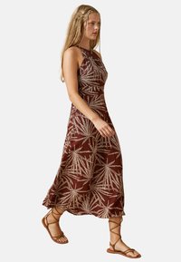 Vestido marrón sin mangas con patrones de hojas blancas, dobladillo acampanado y un corsé ajustado. Combinado con sandalias de tiras marrones.