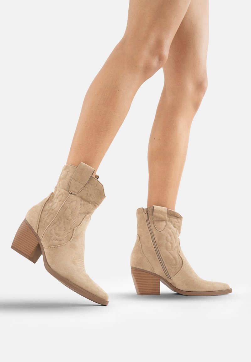 Botines de ante beige con puntera puntiaguda, costuras de estilo occidental, cremallera lateral y tacón de madera apilada.