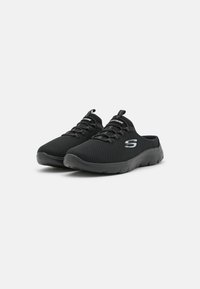 Bottines noires à enfiler avec une tige en mesh, finition texturée, semelle en caoutchouc flexible et un logo sur le côté. Design léger et respirant.