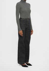 Pull à col roulé gris, jean large taille haute en denim foncé, associé à des talons noirs à bouts pointus. Texture lisse, couture contrastante sur le jean.