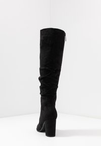 Black over-the-knee boot in soft faux suede, featuring a stretchy shaft, slouchy design, and a block heel for added height.