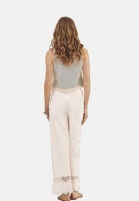 Top corto de punto ligero con un dobladillo con flecos, combinado con pantalones sueltos de color rosa pálido que presentan un detalle de encaje en los tobillos.