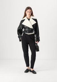 Sort læderjakke med hvid shearling-krave, bælte i taljen og brede ærmer; parret med sorte bukser og sorte loafers.