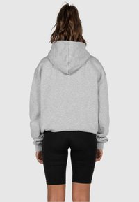 Grauer Kapuzenpullover, lockere Passform, aus Baumwollmischung, mit gerippten Bündchen und Saum, kombiniert mit schwarzen Shorts. Glatte Textur und Kapuzendetail sichtbar.