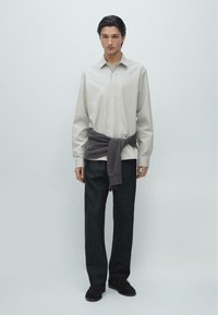 Camicia grigia chiaro con bottoni e leggero bagliore, abbinata a jeans scuri. Maglione grigio scuro legato in vita. Scarpe nere.