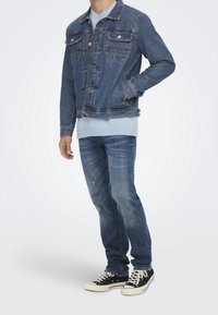 Tummansininen farkkutakki kahdella rintataskulla ja edessä napit, kerroksittain vaaleansinisestä villapaidasta. Yhdistetty haalistuneisiin sinisiin farkkuihin ja mustiin lenkkareihin.