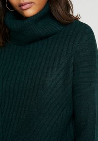 Donkergroen, geribbelde gebreide turtleneck trui met een chunky textuur en een slouchy pasvorm, voorzien van diagonale lijnen en een hoge halsontwerp.