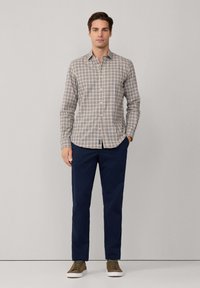 Camisa de botones con un patrón de cuadros en colores azul y beige, combinada con pantalones marinos y zapatillas verde-marrón. Ajuste simple y a medida.