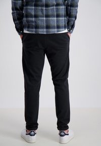 Pantalones de chándal negros ajustados con puños elásticos, combinados con una camisa de franela azul a cuadros. Se ven zapatillas blancas con acentos azules.