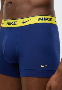 Boxerky z tmavomodrej bavlny so žltým elastickým pásom kontrastujúcej farby, na ktorom je modré logo Nike. Hladká textúra a priliehavý strih.