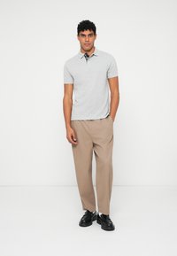 Γκρι κοντομάνικο πόλο μπλουζάκι με γιακά και καρό λεπτομέρεια στον λαιμό, συνδυασμένο με μπεζ παντελόνι σε χαλαρή γραμμή και μαύρα παπούτσια.