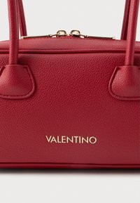 Červená strukturovaná kožená kabelka s dvojitými uchy, zlatými kovovými doplňky a výrazným logem "VALENTINO" na přední straně. Kompaktní obdélníkový design.