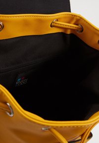 Bolso tipo cubo sintético amarillo con interior de tela negra, equipado con herrajes plateados, cierre de cordón y un bolsillo interior con cremallera.