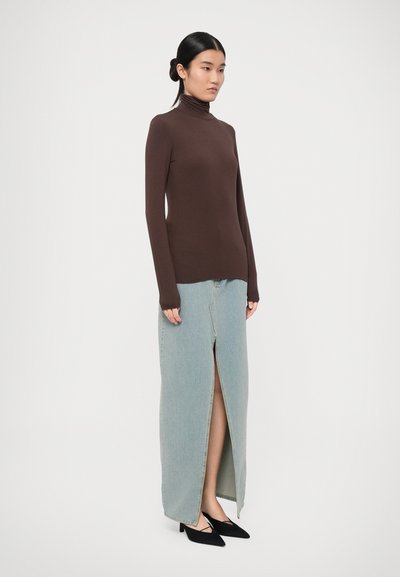 Brown long-sleeve turtleneck top paired with a light blue denim maxi skirt featuring a front slit. Black pointed-toe heels complete the look.