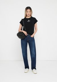 Tricou din bumbac negru cu logo alb, asortat cu blugi drepți albaștri și adidași albi. O geantă crossbody neagră cu un design texturat.