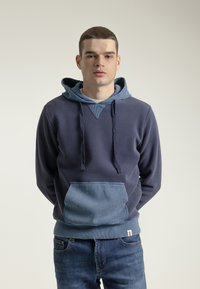 Sudadera de color azul marino con una capucha forrada en un tono de azul más claro y un bolsillo tipo parche. Fabricada con un tejido texturizado, cuenta con un diseño en V y cordones.